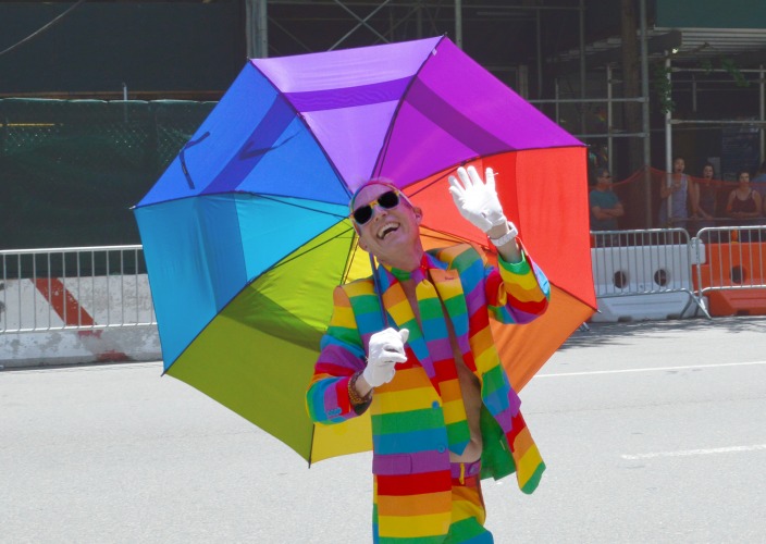 A man in a rainbow costume holds umbrella