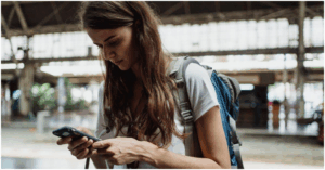 Person focused on their smartphone while wearing a backpack