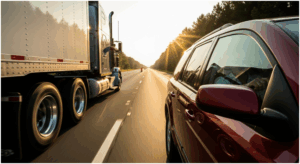 Semi-truck driving alongside a car on a highway during sunset