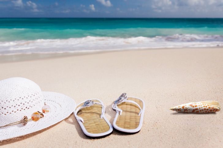 Hat, slippers and seasheel on white beach