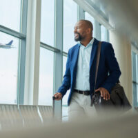 Black man, business and travel at airport on airplane for professional trip, journey or flight. Happy manager walking with suitcase, luggage and bag for boarding, check in or smile at terminal window