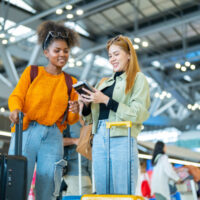 Two woman friends with luggage walking together at Airport terminal.