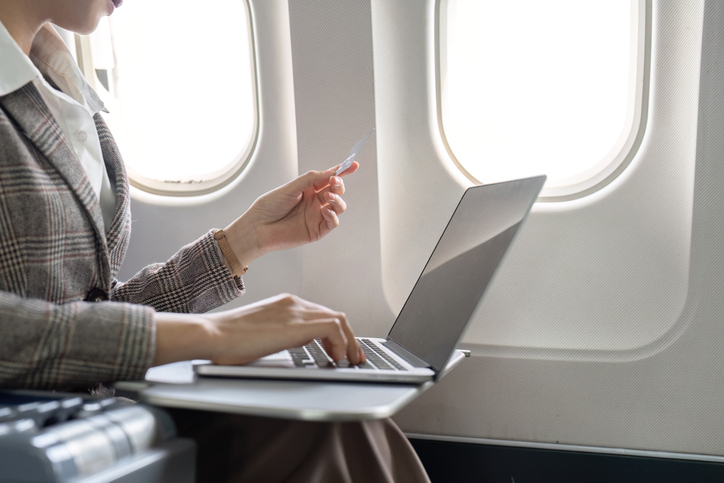 Businesswoman using laptop and credit card for online purchase while seated in airplane