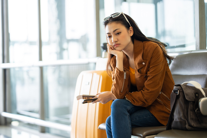 Unhappy young woman traveler disappointed with flight delay or cancelation while waiting at airport terminal, female tourist upset after receiving bad news when sitting at airline lounge.