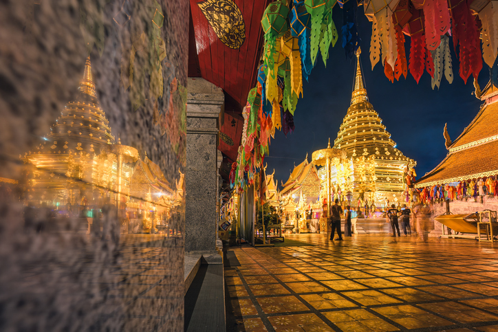 Golden pagoda in Wat Phra That Doi Suthep temple illuminated with tourists visiting to worship at night