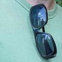one plastic black sunglasses hanging on green t-shirt on man on summer street