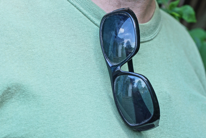 one plastic black sunglasses hanging on green t-shirt on man on summer street