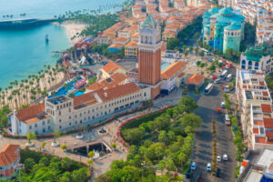 Aerial view of coastal city with Mediterranean style buildings, clock tower, marina, tropical promenade with palm trees and ocean in Sunset Town, Phu Quoc island, Vietnam. Italian architecture in Asia. Travel and touristic destination