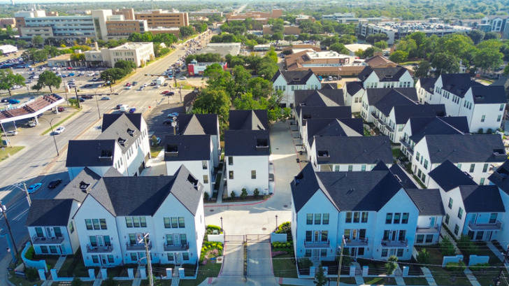 Dense of college campus and commercial buildings from busy Cooper Street intersection in downtown Arlington, Texas. New gated townhomes reflect active development, layered urban infrastructure