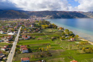 Pogradec Aerial panorama of Pogradec, Albania, showcasing the city spreading along the clear waters of Lake Ohrid, with green farmland, residential neighborhoods, autumn trees, and mountains forming a dramatic natural backdrop.