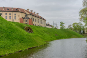 Nesvizh, Belarus - April 28, 2025: Nesvizh Castle. A castle with brick walls, an arched bridge, and a tower under an overcast sky. A medieval castle in Belarus. Fortress with brick walls, arched bridge, and tower under overcast sky
