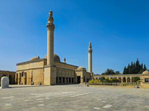 Wide-angle view of the historic Juma Mosque in Shamakhi, Azerbaijan. Featuring its grand stone courtyard, majestic minarets, and central dome against a clear blue sky. This landmark represents centuries of Islamic heritage and architectural restoration in the Caucasus.