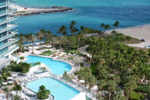 High-angle view of a luxury resort pool deck featuring lush palm trees directly beside the oceanfront in Miami Beach