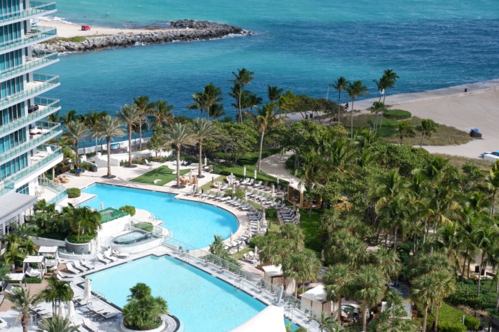 High-angle view of a luxury resort pool deck featuring lush palm trees directly beside the oceanfront in Miami Beach