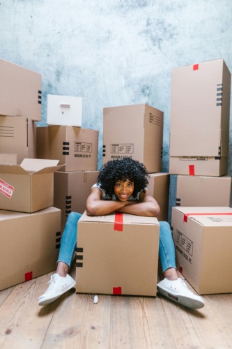 person sitting by a cardboard box surrounded by many other stacked boxes